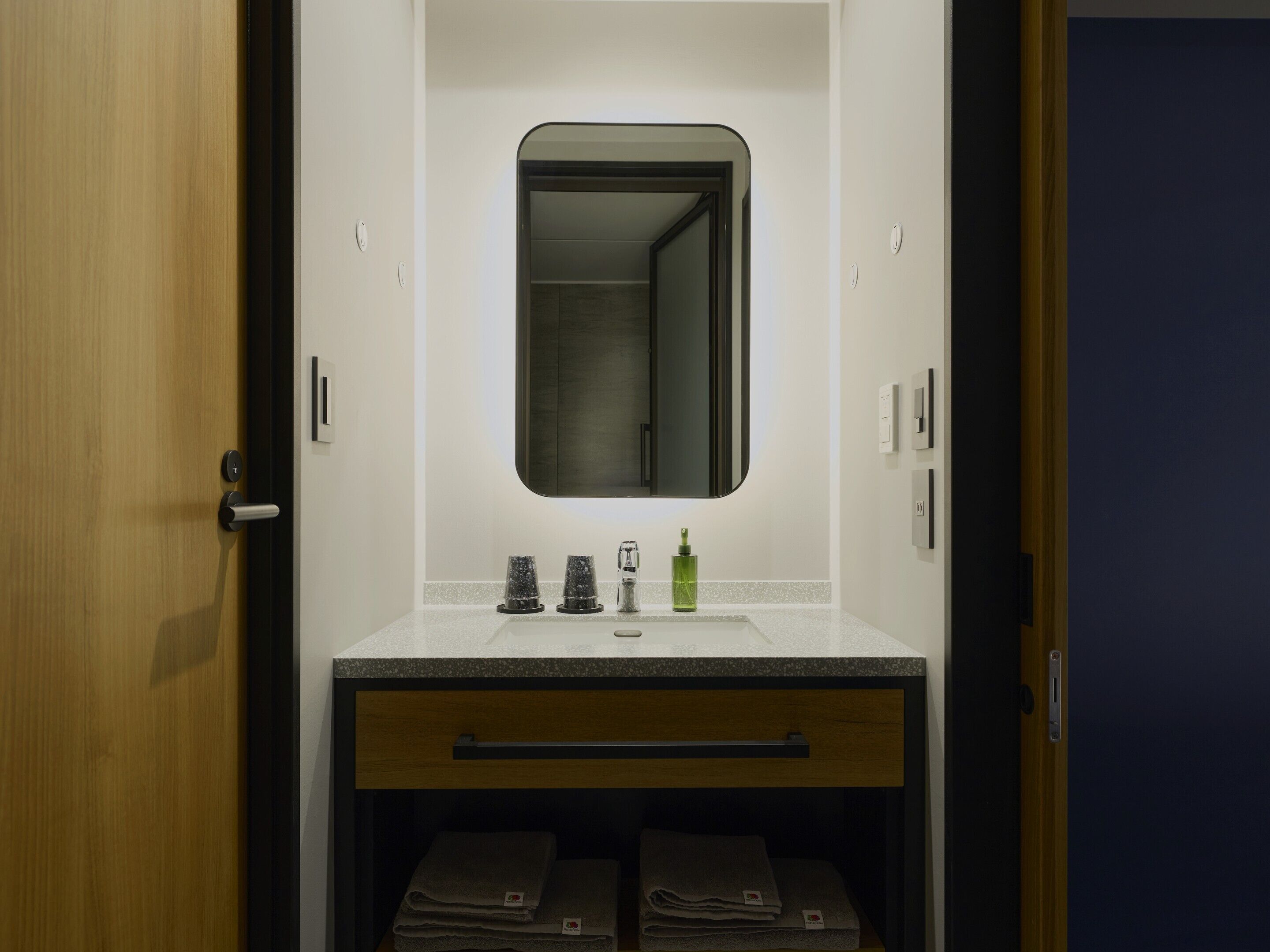 A bathroom with a wooden door, a white sink with a mirror above it, and a towel rack below.