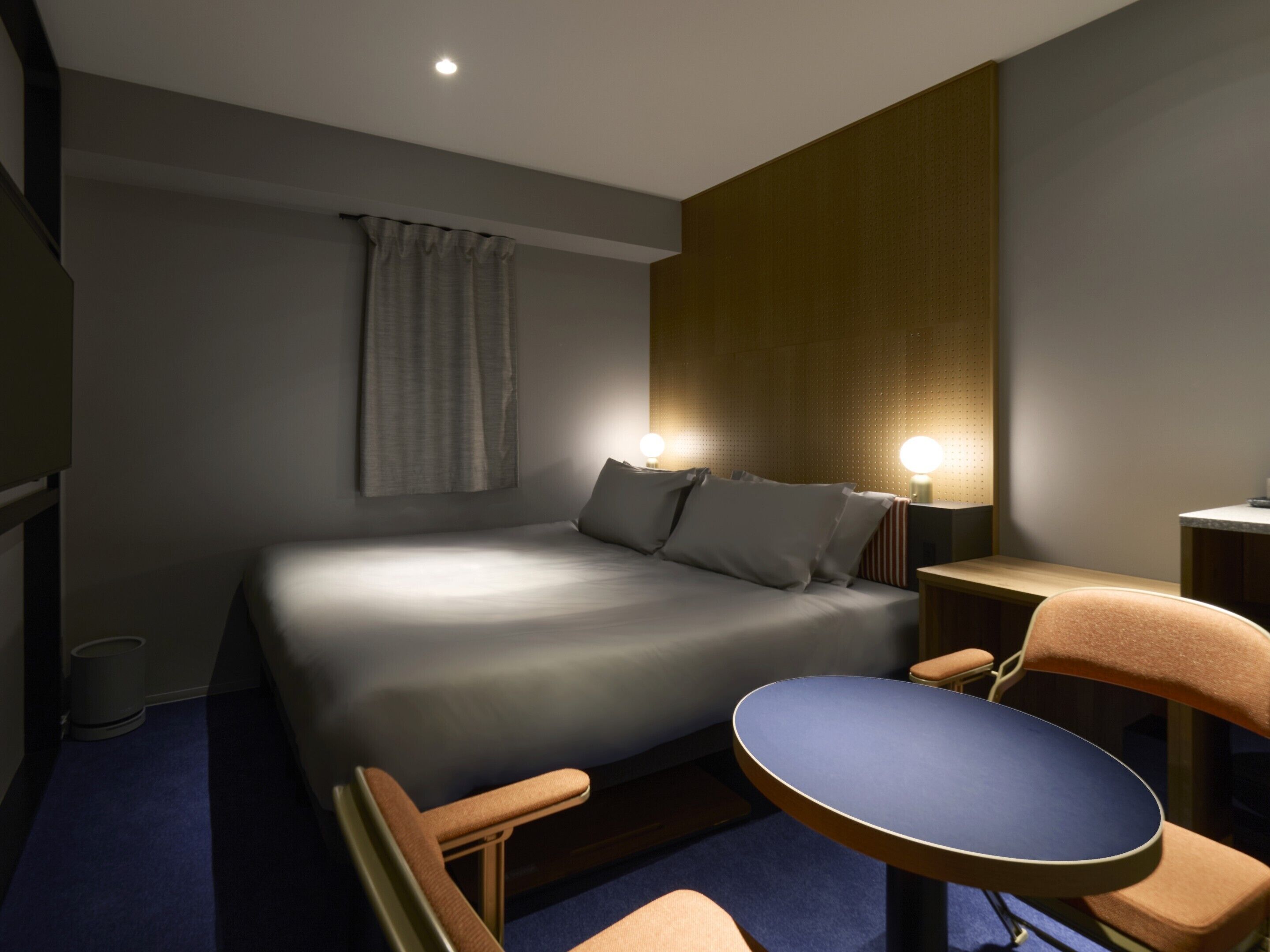A hotel room with a bed, bedside tables, a desk, and a chair.