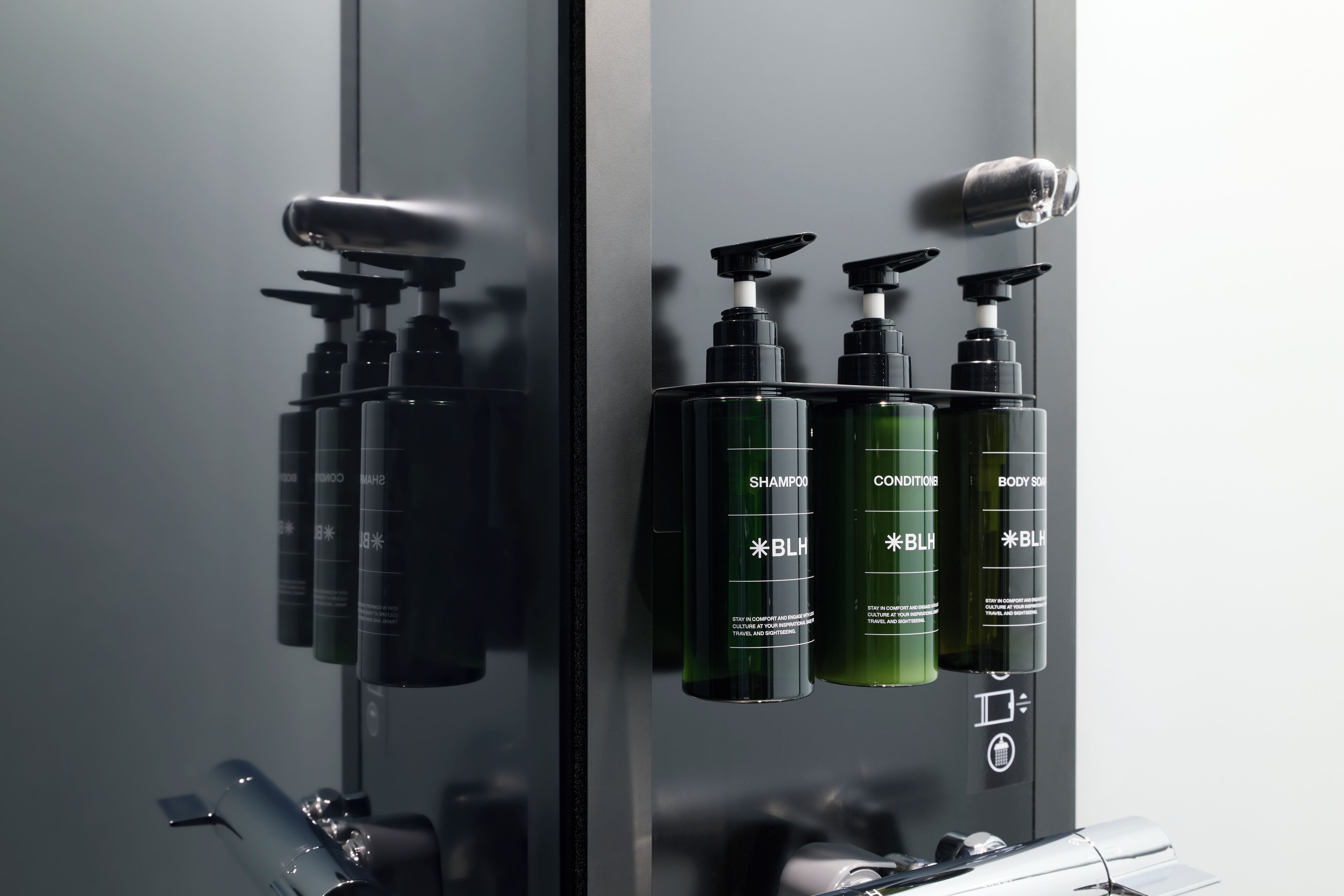 A bathroom with a mirror, a sink, and three bottles of BLH shampoo and conditioner.