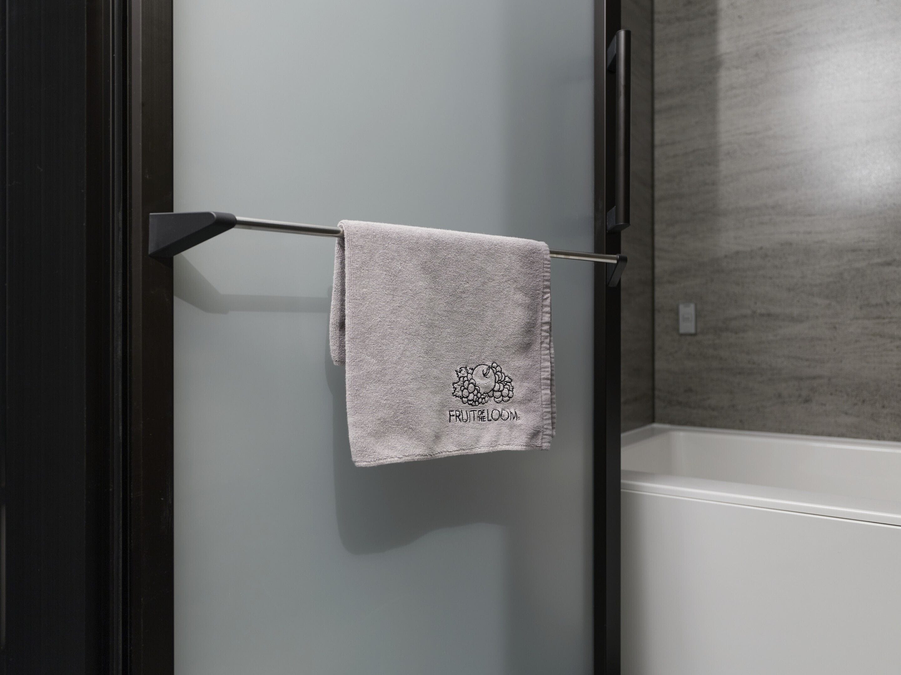 Une serviette est suspendue à un porte-serviettes en métal dans une salle de bain dont les murs sont gris et qui contient une baignoire blanche.
