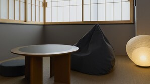 A room with tatami flooring, a round wooden table, a black bean bag, a woven lamp, and shoji screens.