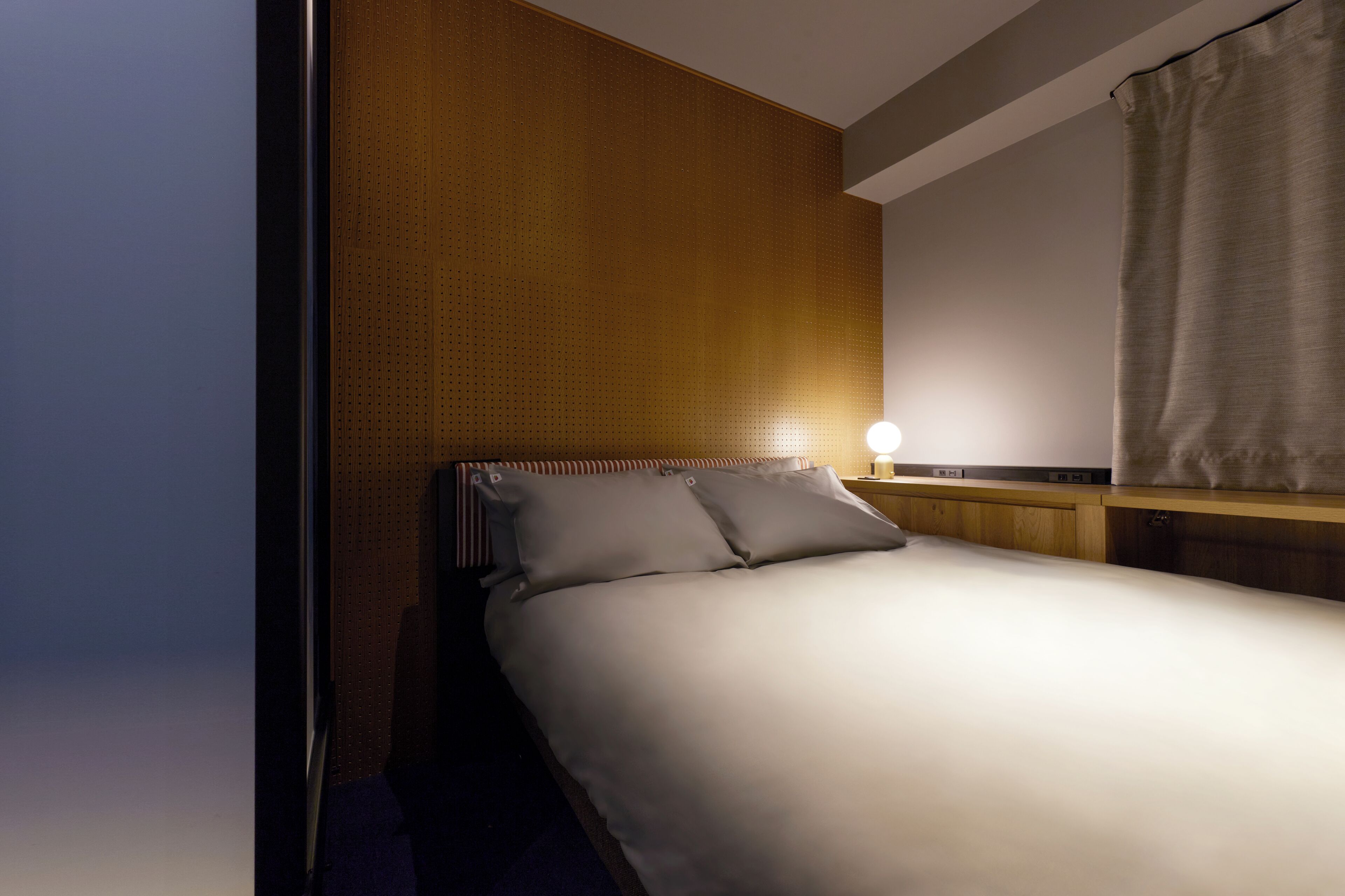 Une chambre d’hôtel avec un lit, une table de chevet, une lampe et un rideau.