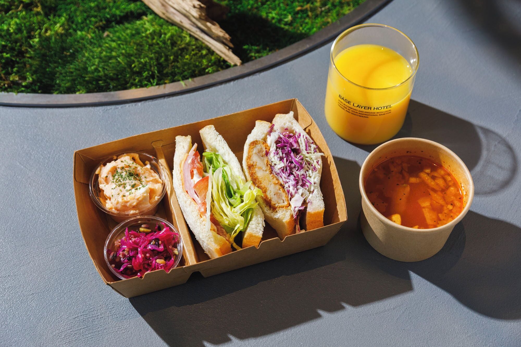 Una comida con sándwiches, ensalada de col y un tazón de sopa, junto con un vaso de jugo de naranja sobre una mesa.
