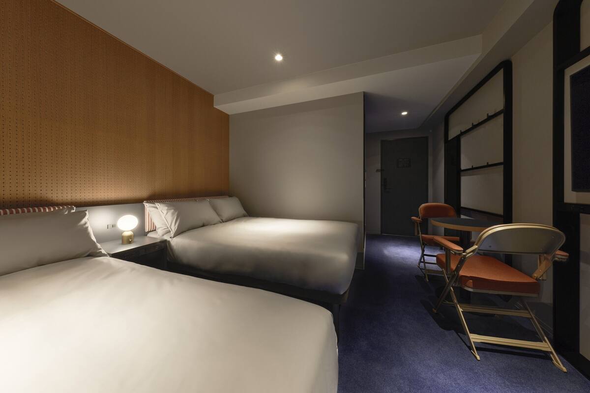 A hotel room with two beds, a desk, a chair, and a small table.