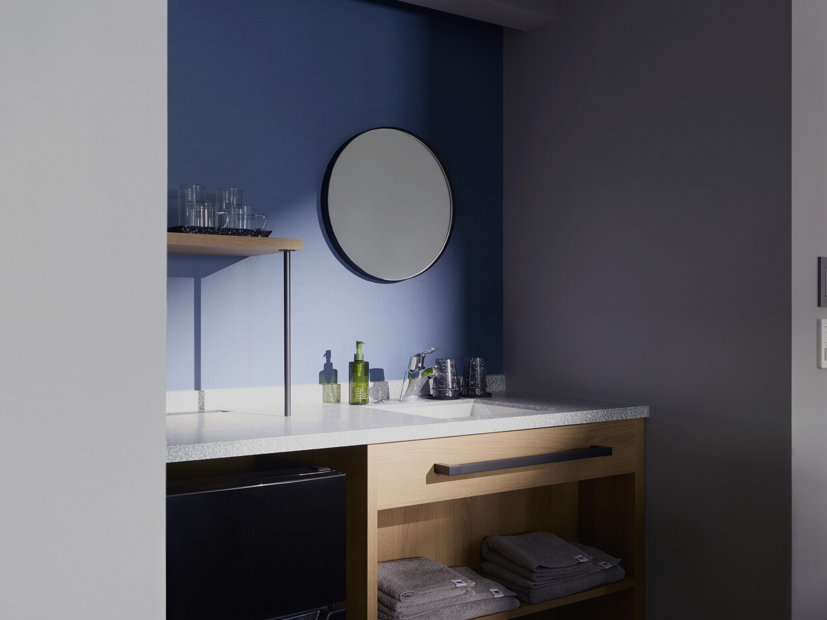 Un baño moderno con un espejo redondo, un lavabo y una repisa con artículos de aseo.