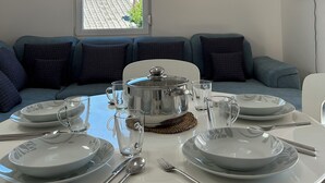 En matplats med ett runt bord för fyra personer, ett stort fönster med utsikt över byggnader, en platt-TV som är monterad på väggen och en soffa med kuddar.