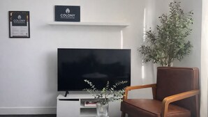 Un soggiorno moderno con una TV a schermo piatto, una poltrona in pelle marrone, un tavolino da caffè bianco e una pianta in vaso.