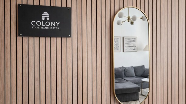 Un cartello con su scritto 'Colony Stays Manchester' su un muro di legno.