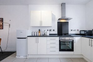 A modern kitchen with white cabinets, a built-in oven, a microwave, and a stainless steel range hood. - Manchester Apartment Sleeps 4 + Free Parking (Salford)
