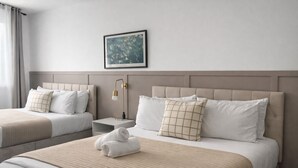 Una camera d'albergo con due letti, un comodino con una lampada, un quadro appeso al muro e un asciugamano arrotolato sul letto.