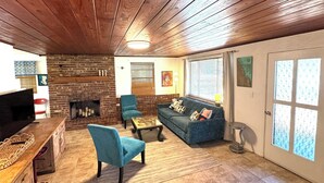 Ein gemütliches Wohnzimmer mit Kamin aus Backsteinen, Holzbalkendecke und einem blauen Sofa.
