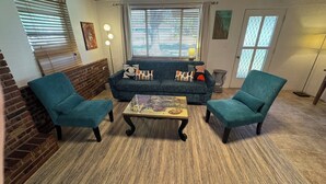 Ein gemütliches Wohnzimmer mit einem blauen Sofa, zwei gleichfarbigen Sesseln, einem Couchtisch mit einer dekorativen Mittelstück und einer Wand aus Ziegelsteinen.