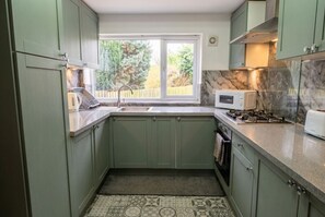 A compact kitchen with a window, a microwave, a stove, and a sink. - Spacious detached home with fireplace, BBQ, and parking (West Yorkshire)
