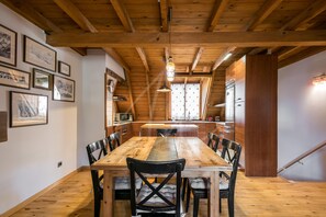 A wooden dining table with chairs, a kitchen area with a refrigerator, and framed pictures on the walls.