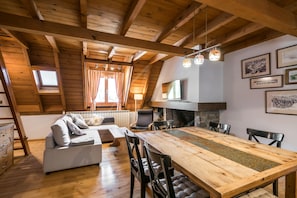 A cozy loft-style room with a wooden ceiling, a dining table, and a sofa.