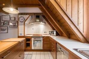A compact kitchen with wooden cabinets, a built-in oven, a microwave, and a clock on the wall.