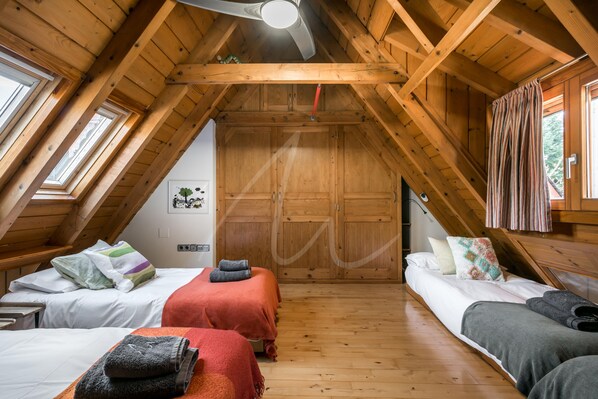 A cozy attic bedroom with wooden beams, two beds, and a sloped ceiling.