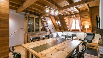 Een houten eethoek met een grote tafel en stoelen, een kast met glazen deuren, en een gezellige zithoek met kussens.