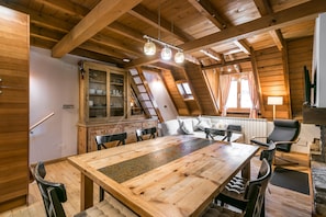 A wooden dining area with a large table and chairs, a cabinet with glass doors, and a cozy seating area with cushions.