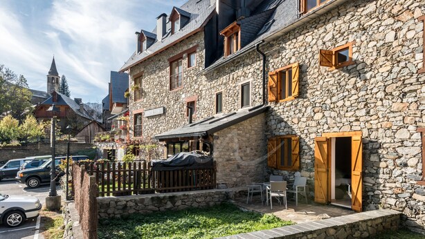 A stone building with a balcony, outdoor seating, and a car parked in front. - Casa Unhòla by SeaMount Rentals (Unha)