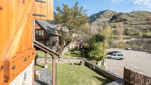 A rustic wooden building with a stone foundation, a stone staircase, and a view of a parking lot and hills in the background. - Casa Unhòla by SeaMount Rentals (Unha)