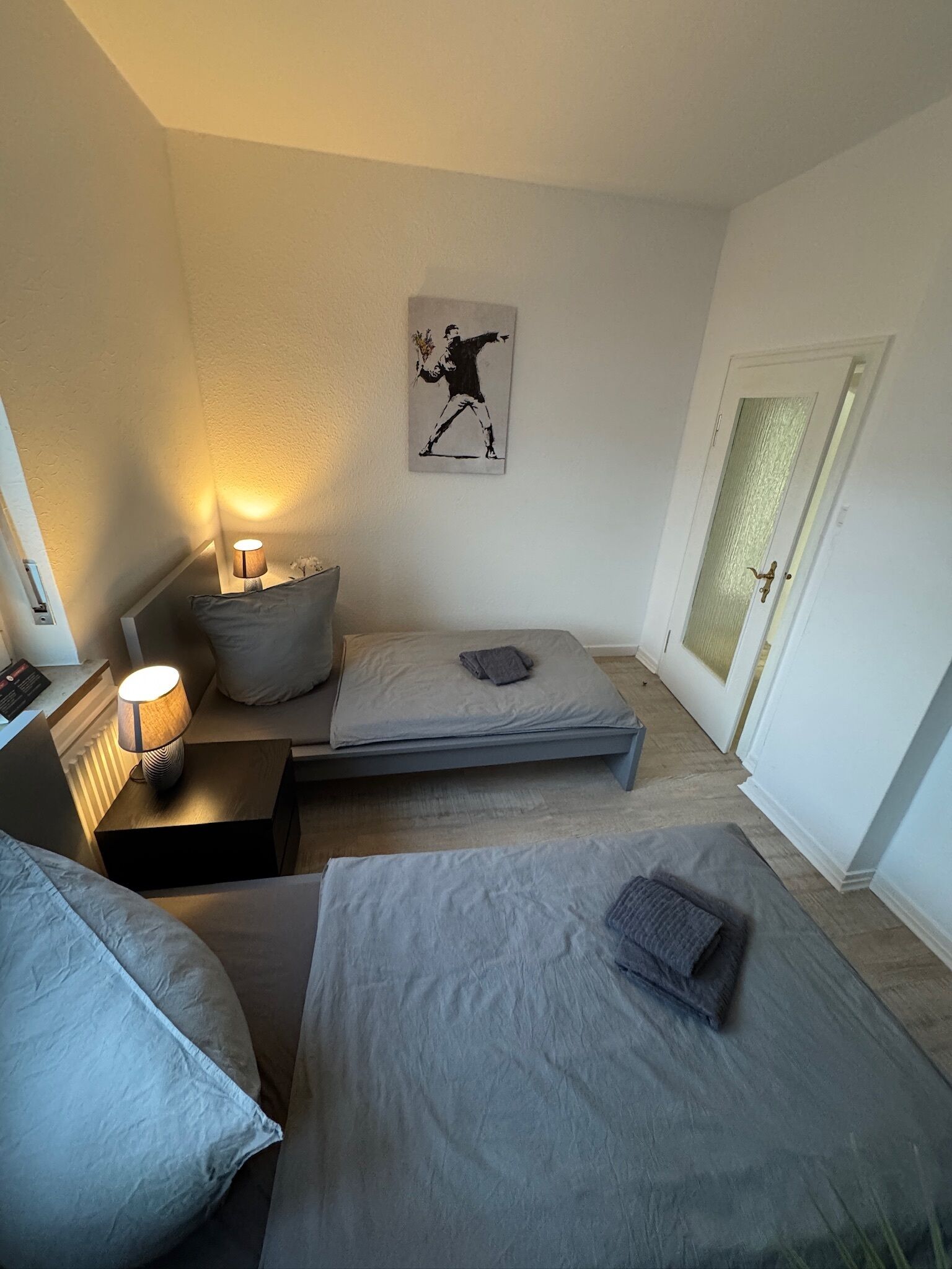 Ein Schlafzimmer mit einem Bett, Nachttischen, einer Lampe, einer Wanduhr und einer Tür.