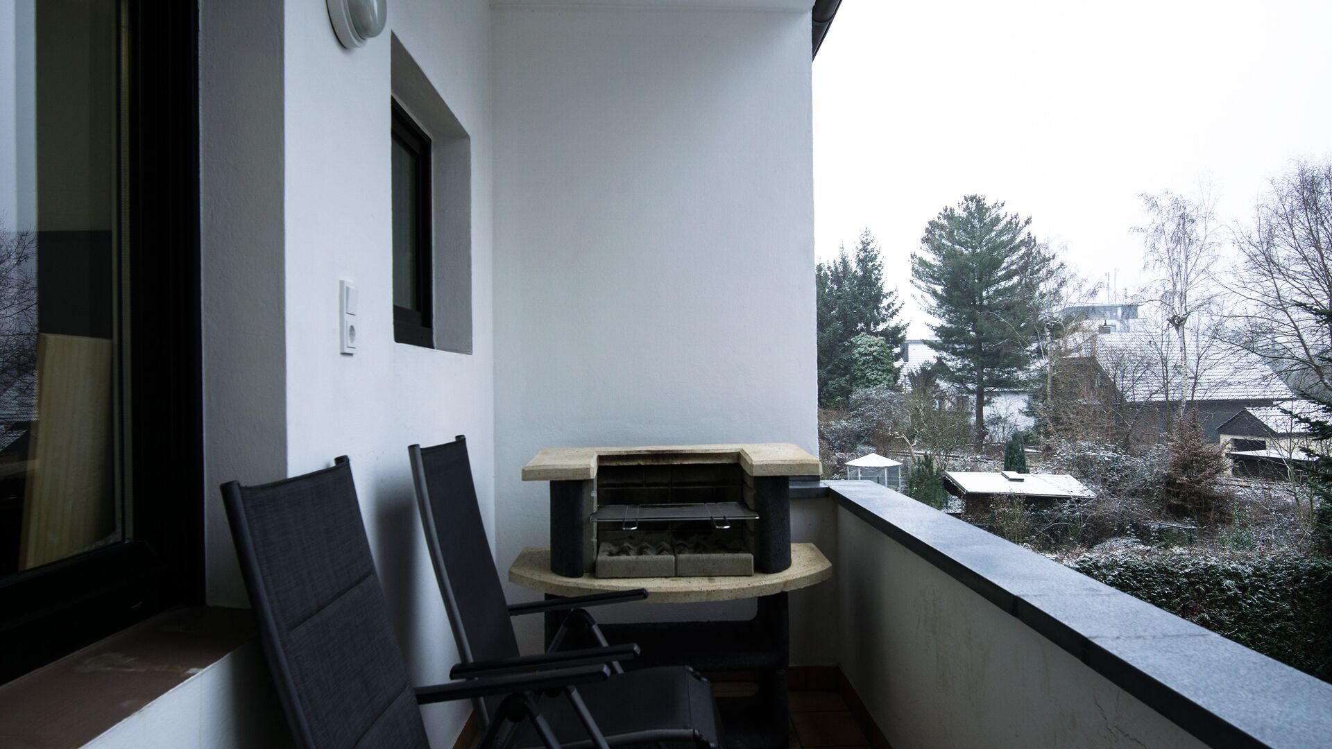 A balcony with a built-in grill, chairs, and a view of a snowy landscape.