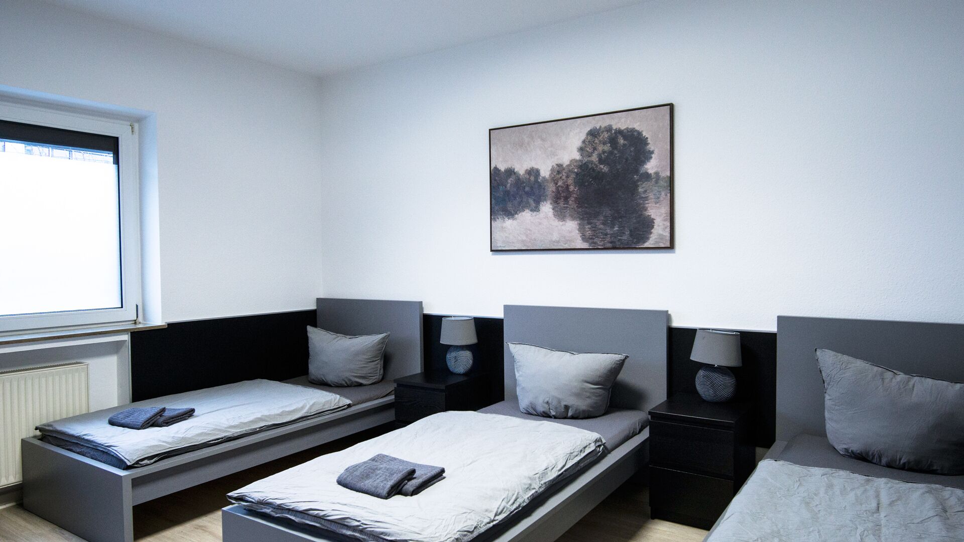 A room with two single beds, a window, a painting, and a radiator.