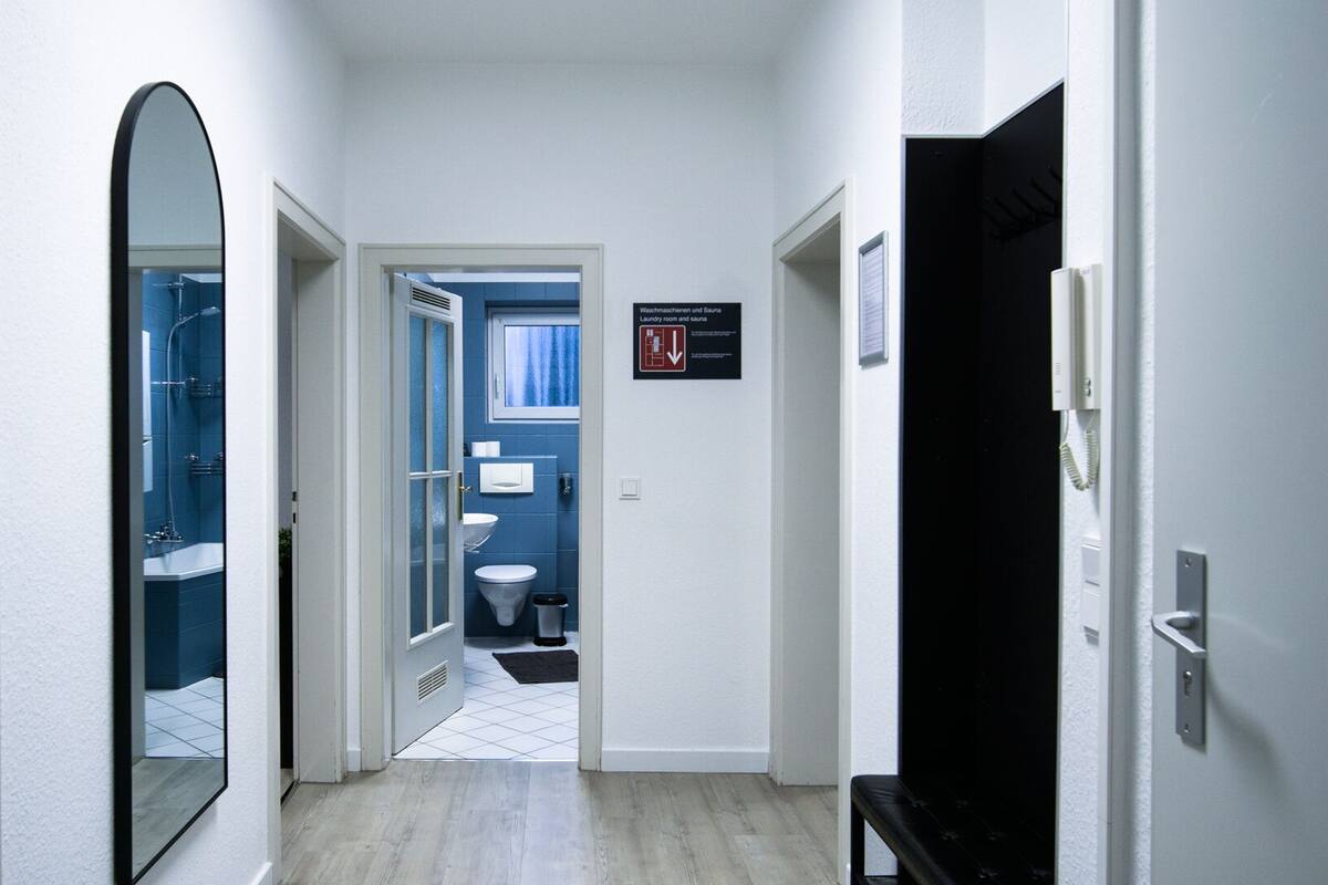 Un couloir mène à une salle de bain équipée d’un miroir, à une buanderie et à un sauna, et il y a un banc.