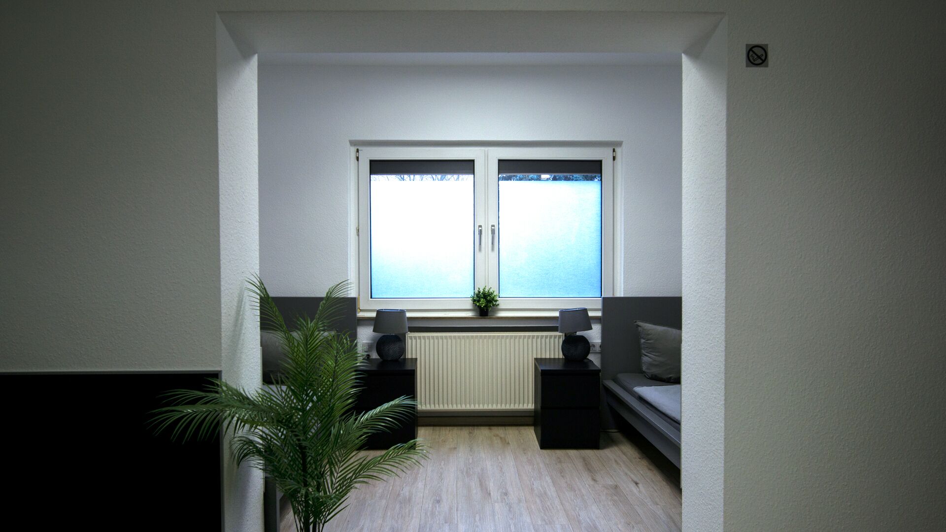 A room with a window, radiator, sofa, two side tables, and a potted plant.