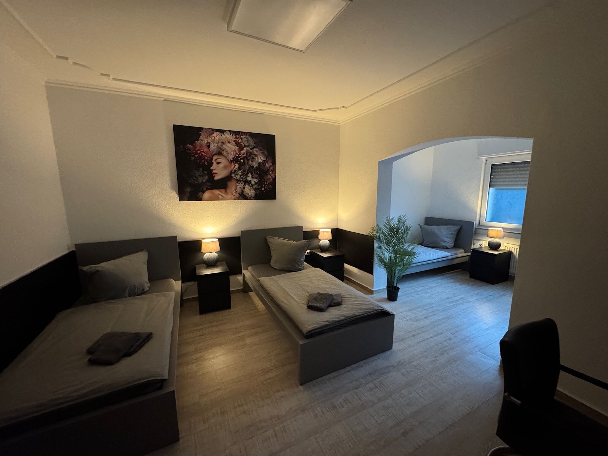 Ein modernes Hotelzimmer mit zwei Betten, einem großen Gemälde, einer Topfpflanze und Blick ins Freie.