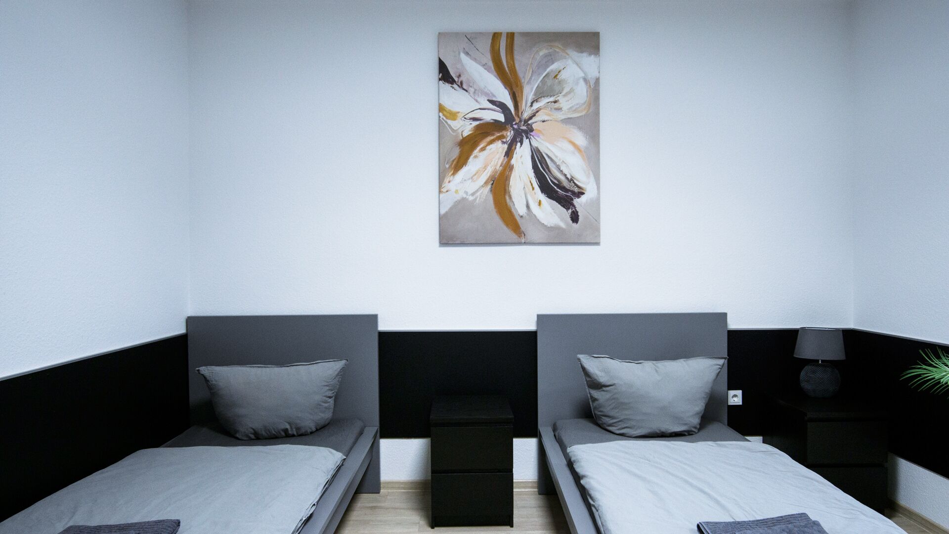 A room with two beds, a painting on the wall, a nightstand, and a lamp.