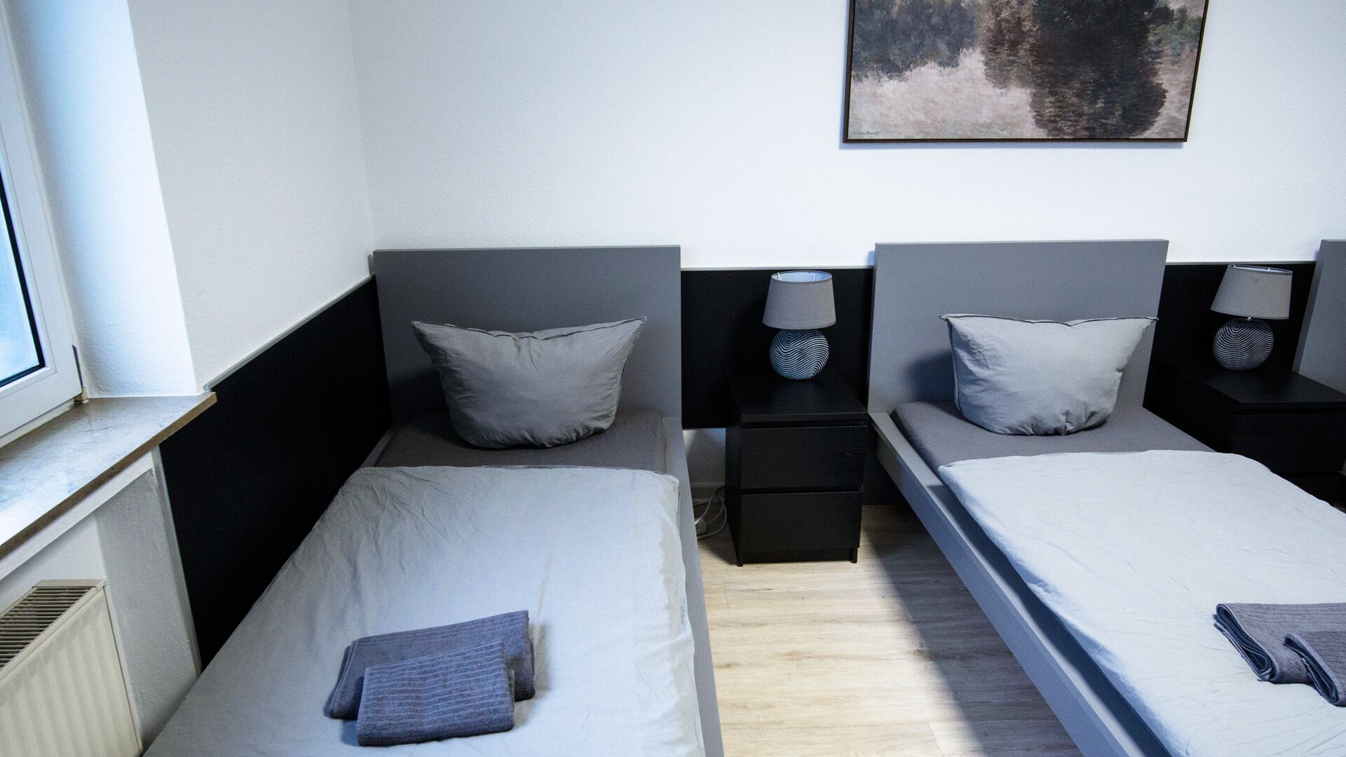 Ein Doppelzimmer mit zwei Betten, einem Fenster, einem Gemälde und Nachttischen mit Lampen.