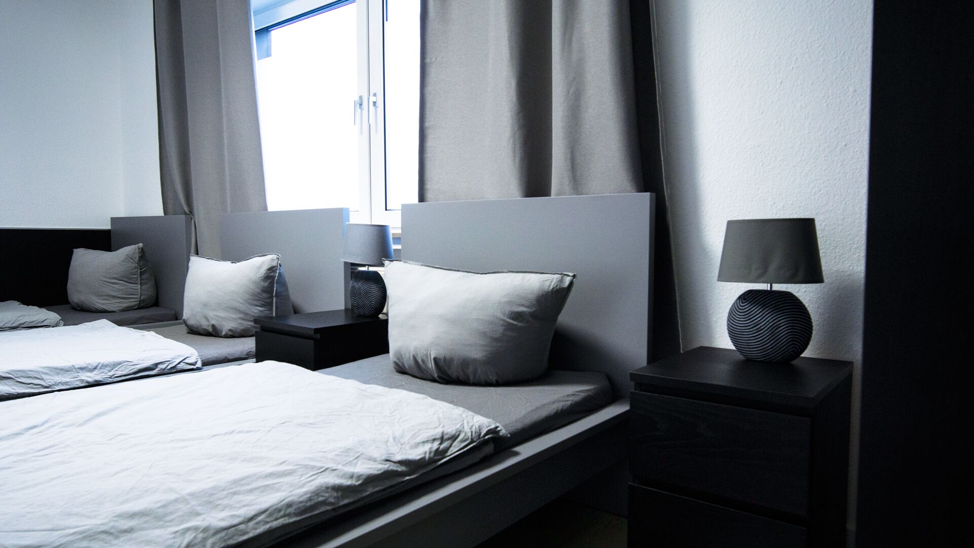A modern hotel room with a large bed, two bedside tables, a lamp, and a window with curtains.