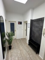 Um corredor com luminária no teto, planta em vaso, um banco e placa indicando lavanderia e sauna.