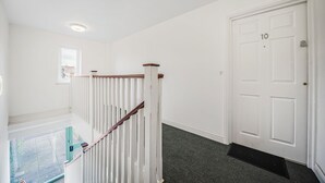 A clean, white hallway with a wooden staircase, a door labeled "10", and a small window. - The Cosy Spot- Contractor Friendly- Free Parking (Clapham)