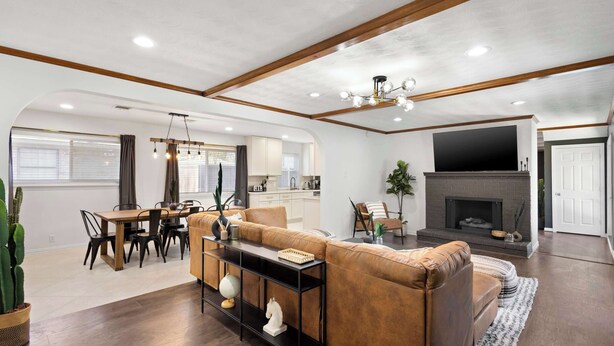 A spacious living room with a brown leather sofa, a dining area with a wooden table and chairs, a fireplace, and a kitchen in the background. - 6BD/3.5BA Modern Rustic Retreat | Yard, Pool & BBQ (Richardson)