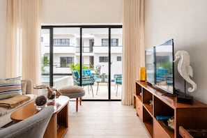 A modern living room with a sofa, TV, and a balcony with outdoor furniture.