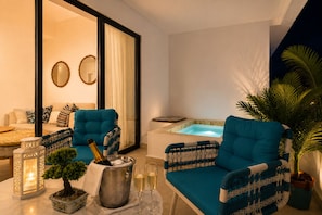 A modern living room with a sofa, two armchairs, a small table with a bottle of champagne, glasses, and a decorative plant.