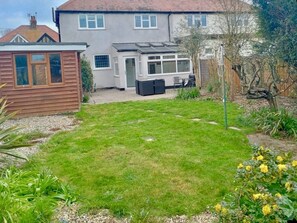 A residential backyard with a lawn, a shed, and a house with a tiled roof.