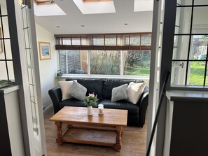 A cozy living room with a black leather sofa, a wooden coffee table, and a large window with blinds.