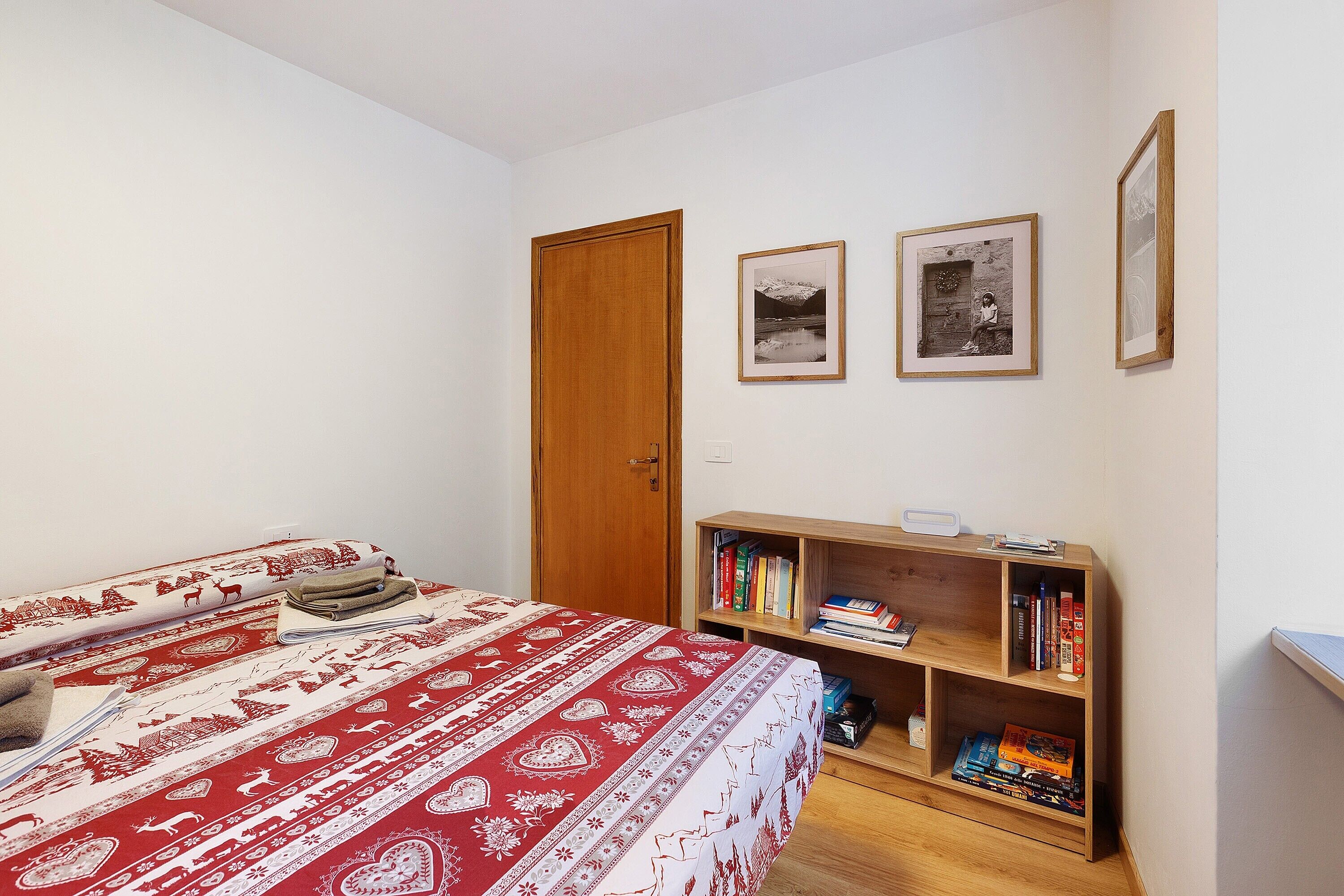 A bedroom with a bed, a wooden bookshelf, and two framed pictures on the wall.