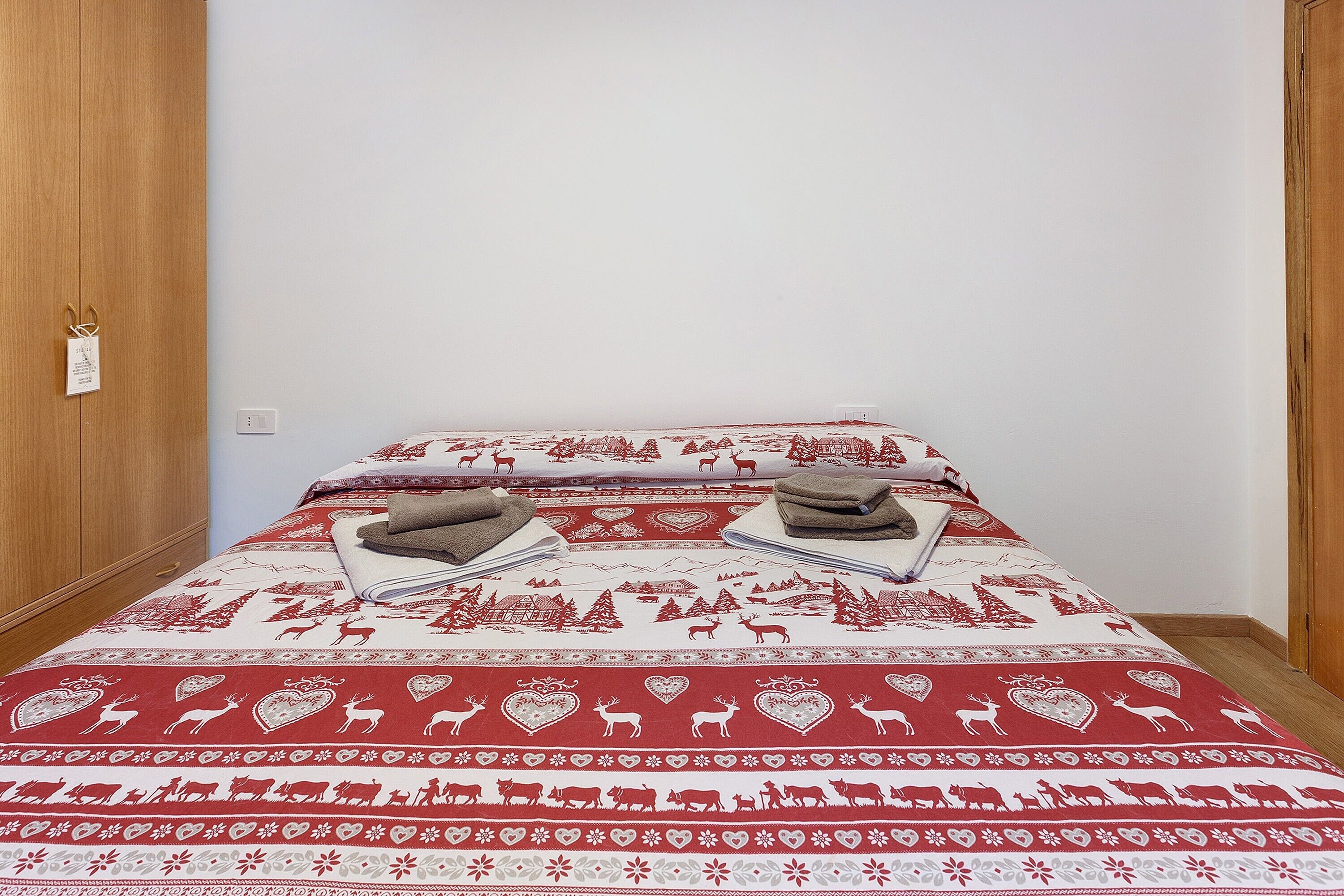 A bed with a patterned bedspread, two towels, and a wooden wardrobe.