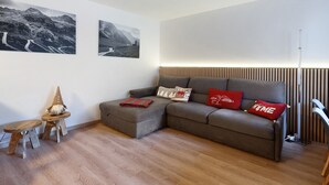 Ein modernes Wohnzimmer mit einem grauen Ecksofa, zwei hölzernen Hockern und einem kleinen Tisch mit einem dekorativen Gegenstand.
