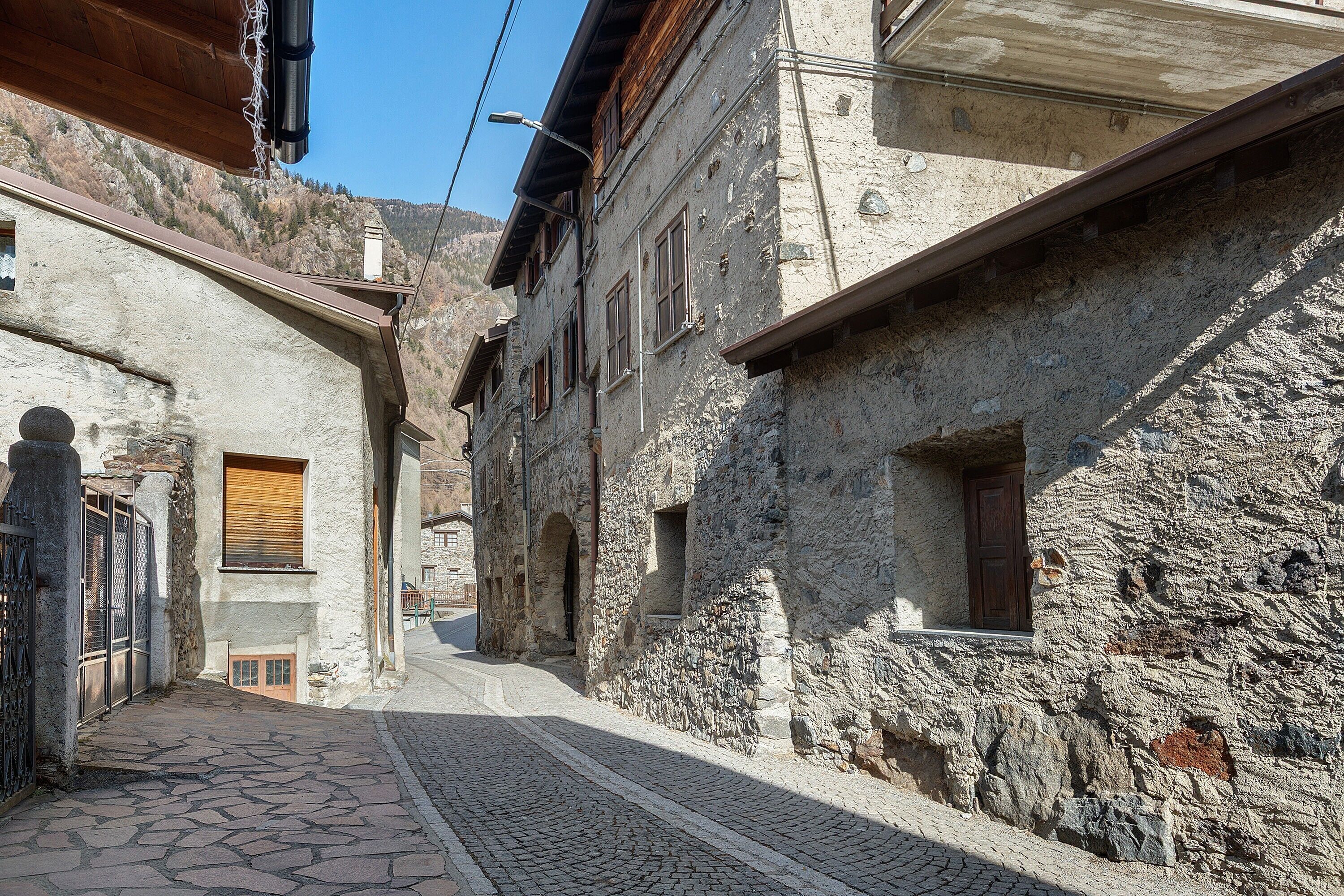A narrow cobblestone street flanked by historic stone buildings with arched doorways and wooden shutters.