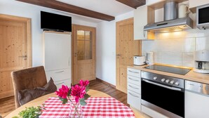 Een keuken met houten kastjes, een Bosch oven, een televisie en een tafel met een rood-wit geruit tafelkleed en bloemen.