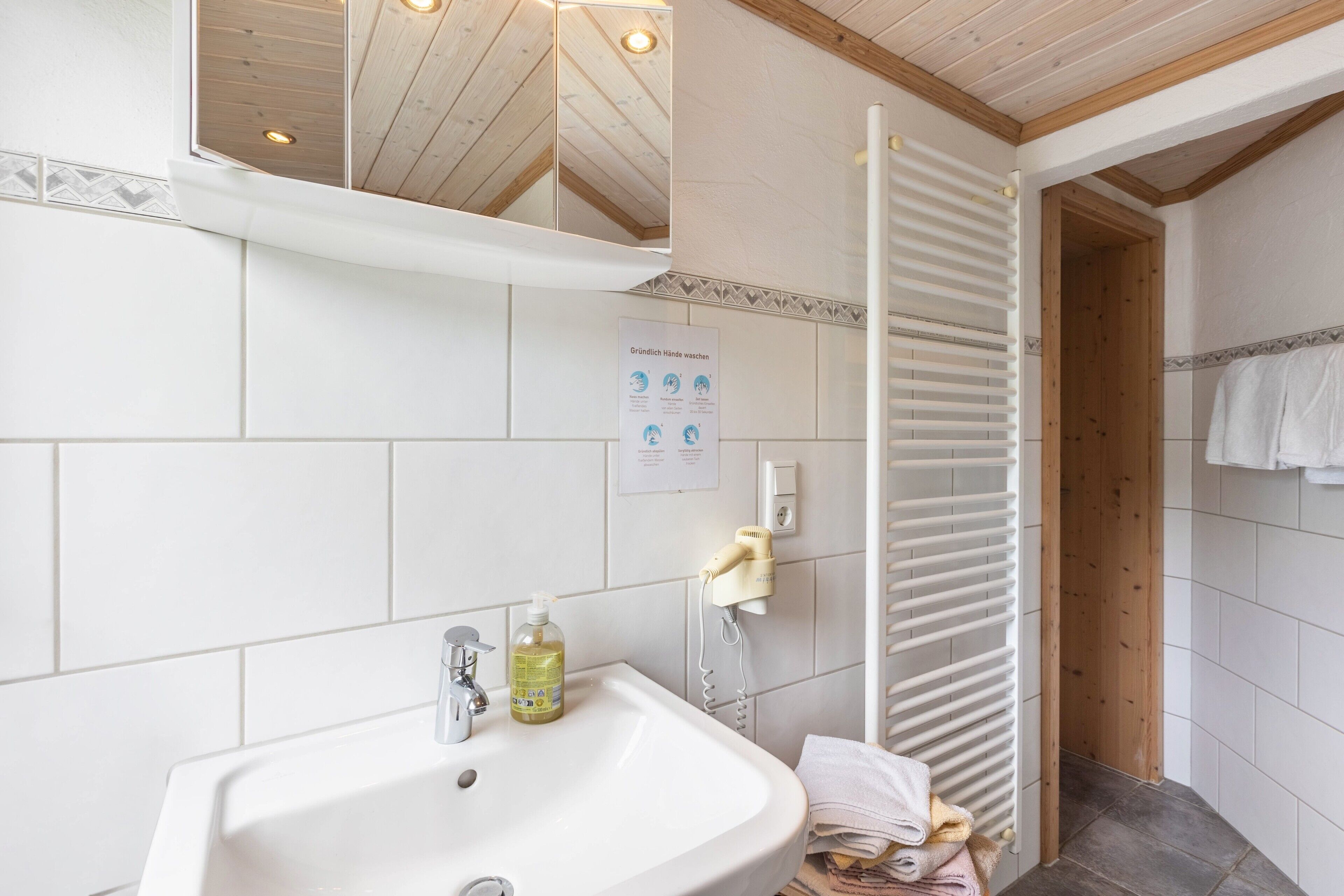 Un baño con lavamanos, espejo, toallero y puerta de madera.