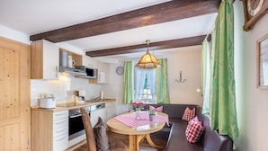 Een kleine keuken met houten kastjes, een eettafel met een rood-wit geruit tafelkleed en een bank met geruite kussens.