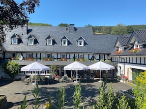 A building with a gabled roof, multiple windows, outdoor seating with umbrellas, and a courtyard.
