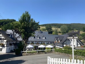 A traditional building with a sign reading 'Pension Pohl,' surrounded by a white picket fence, with a clear view of the surrounding landscape.